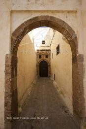 Image du Maroc Professionnelle de  Dans une rue des Habous, la succession des balèvres, moulure, arches, portiques et autres éléments décoratifs, projetent les visiteurs dans l’ardeur avec un élan de force et de fierté d’une époque révolue. Conçu par les architectes Auguste Cadet et Edmond Brion d’après l’ébauche d’un premier plan-masse dû à Albert Laprade, le quartier fait partie des endroits les plus pittoresques de Casablanca, il fut La construction n’avait commencé qu’après la première guerre mondiale. Situé près du Palais Royale, ce joyau architectural fait partie du patrimoine architectural de la ville, Samedi 8 Novembre 2008. Au centre le minaret de La mosquée Ben Youssef. (Photo / Abdeljalil Bounhar)
